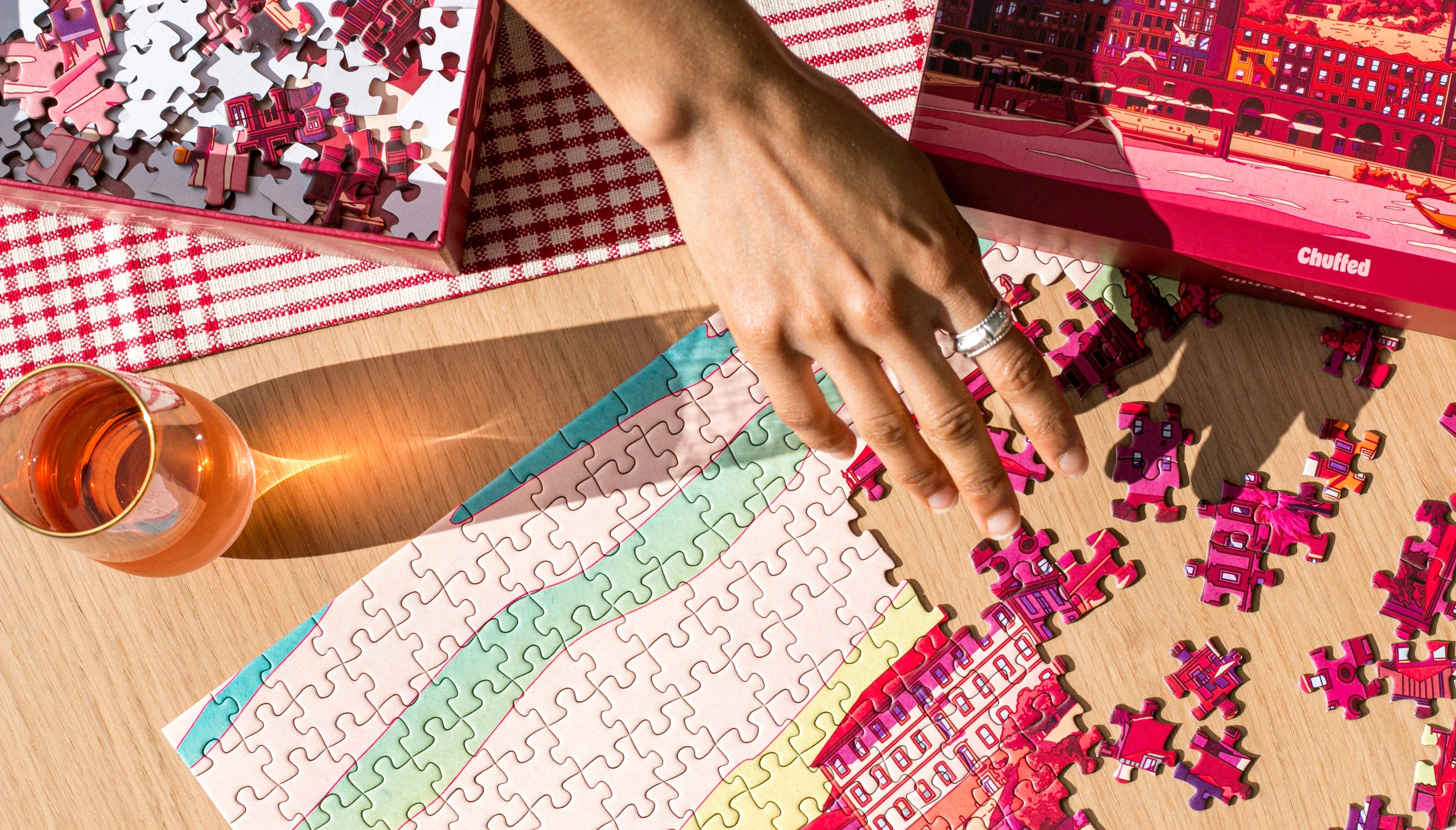 A hand assembling Porto in Red on a sunlit table beside its box